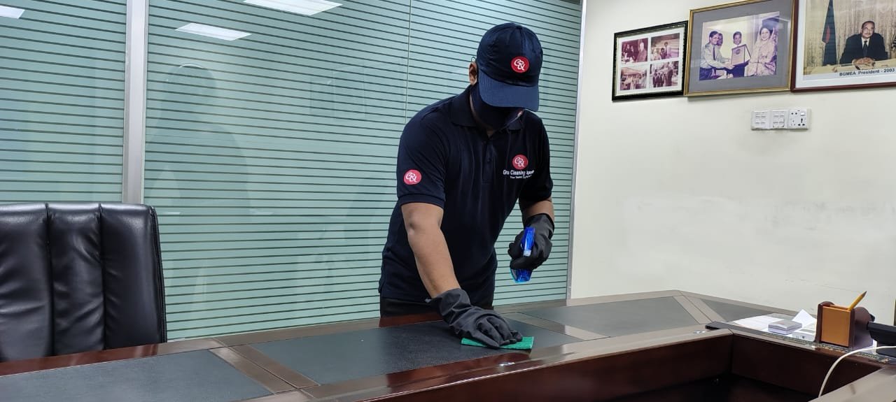 GURU® employee cleaning the top of a nightstand in a white bedroom